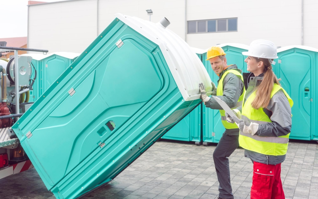 Two workers transporting portable toilet