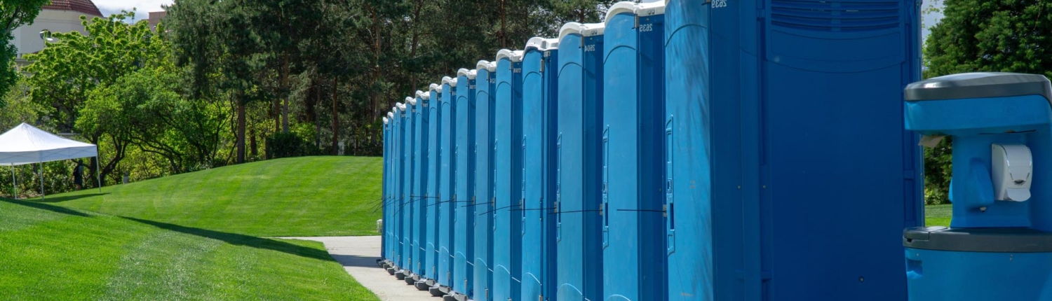 Side view of a row of blue porta potties next to a grassy area