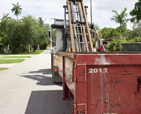 Side view of a construction dumpster being unloaded from truck at residential construction site